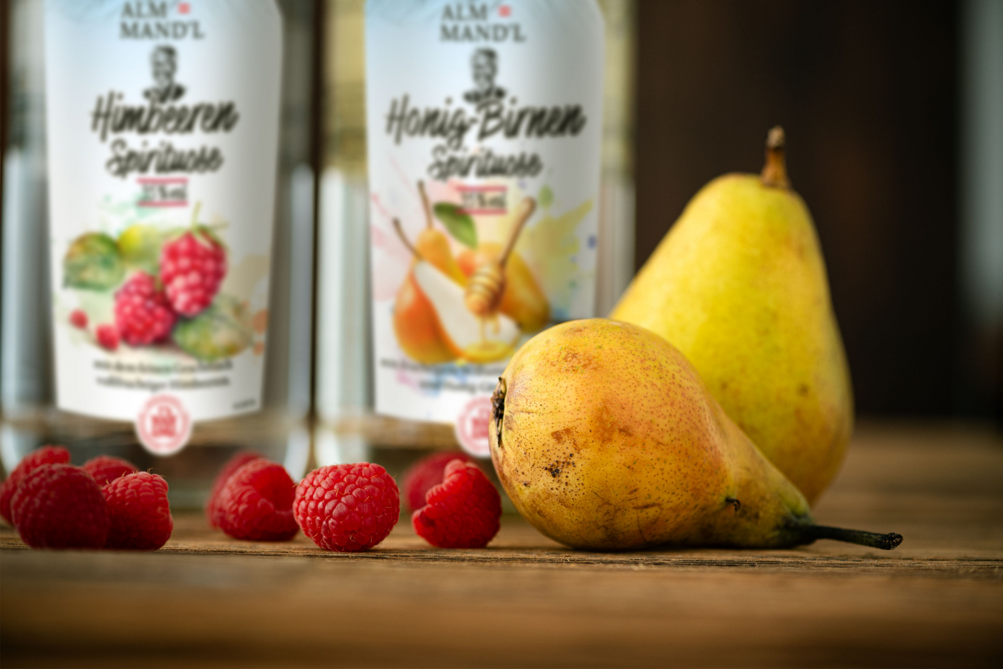 Birnen und Himbeeren liegen auf einem Holzuntergrund mit Spirituosen-Flaschen im Hintergrund.